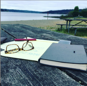 close-up of a notepad, pen and eyeglasses on a weatherbeaten picnic table ona deserrted beach